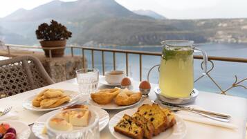 Una mesa servida con varios pasteles, una jarrón de limonada y una vista panorámica de las montañas al fondo.