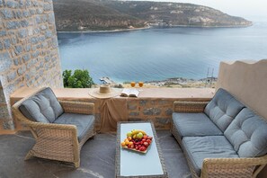 A balcony with wicker furniture, a table with fruit, and a view of the sea. - King Suite with Panoramic Sea View | Akrolithi Guesthouse (East Mani)