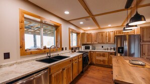 A modern kitchen with wooden cabinets, stainless steel appliances, and a large window.