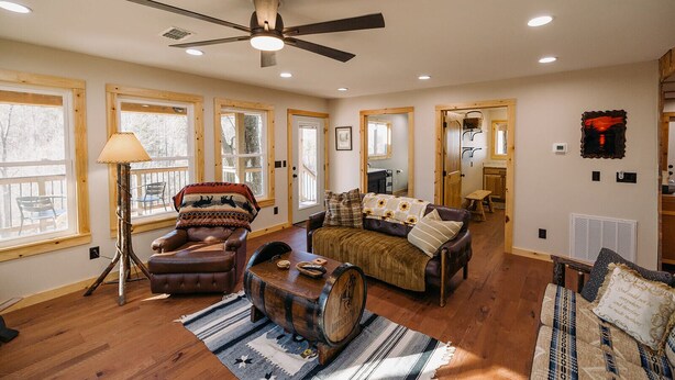 A spacious living room with a large ceiling fan, wooden flooring, and a cozy fireplace.