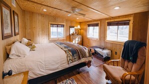 A wooden cabin bedroom with a bed, a chair, a desk, and a window.