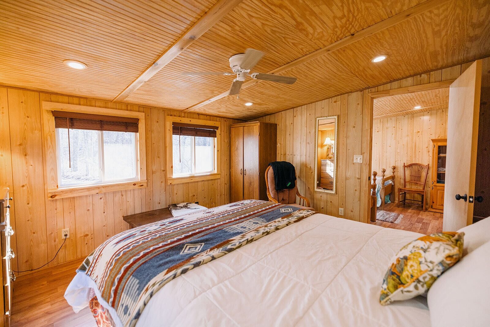 A wooden-paneled bedroom with a bed, a chair, and a ceiling fan.