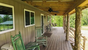 A covered porch with wooden beams, a ceiling fan, and a view of greenery outside.