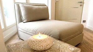 A bedroom with a beige sofa, a lit candle on a patterned table, and a door in the background. - Beautiful apartment - Galeries Lafayette (Paris)