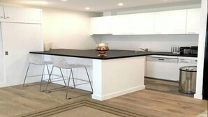 A modern kitchen with white cabinets, a black countertop, and a small island with bar stools. - Beautiful apartment - Galeries Lafayette (Paris)