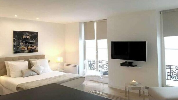 A hotel room with a bed, a TV mounted on the wall, and a balcony with a railing. - Beautiful apartment - Galeries Lafayette (Paris)
