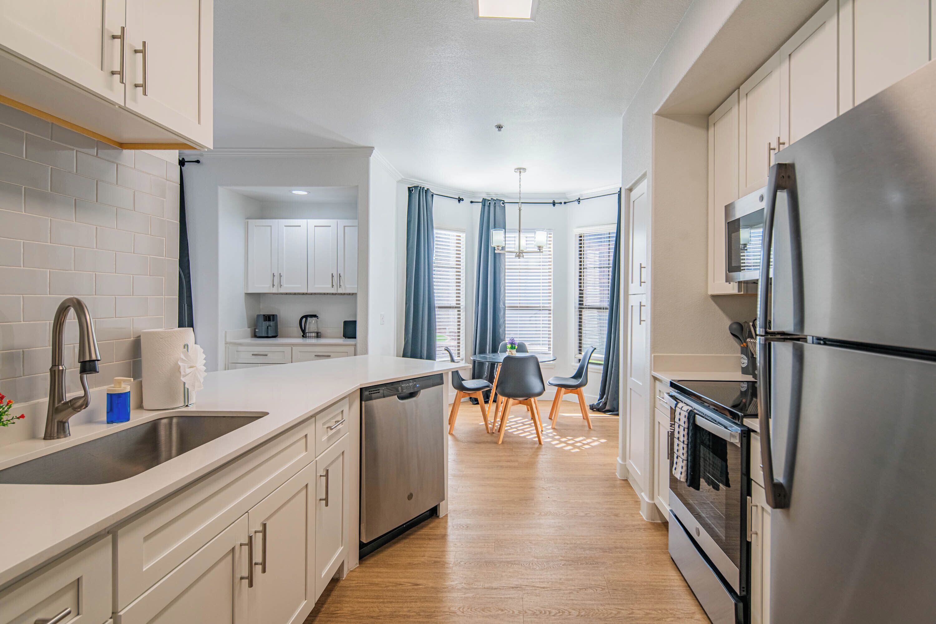 A modern kitchen with white cabinets, stainless steel appliances, and a wooden dining area.