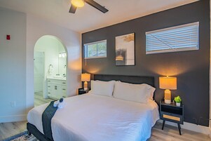 A bedroom with a large bed, two bedside tables with lamps, a headboard, and artwork on the wall.