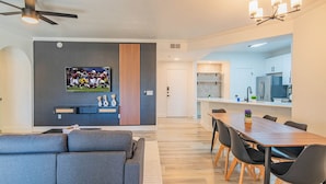 A modern living room with a gray sectional sofa, a flat-screen TV mounted on a gray accent wall, and a wooden accent wall. - ROVE LIVING/KB - Zone (Glendale)