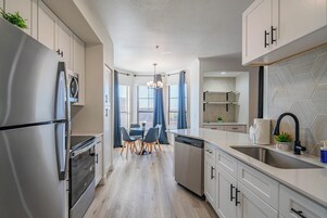 A modern kitchen with stainless steel appliances, a dishwasher, and a sink. There is a dining area with a table and chairs.