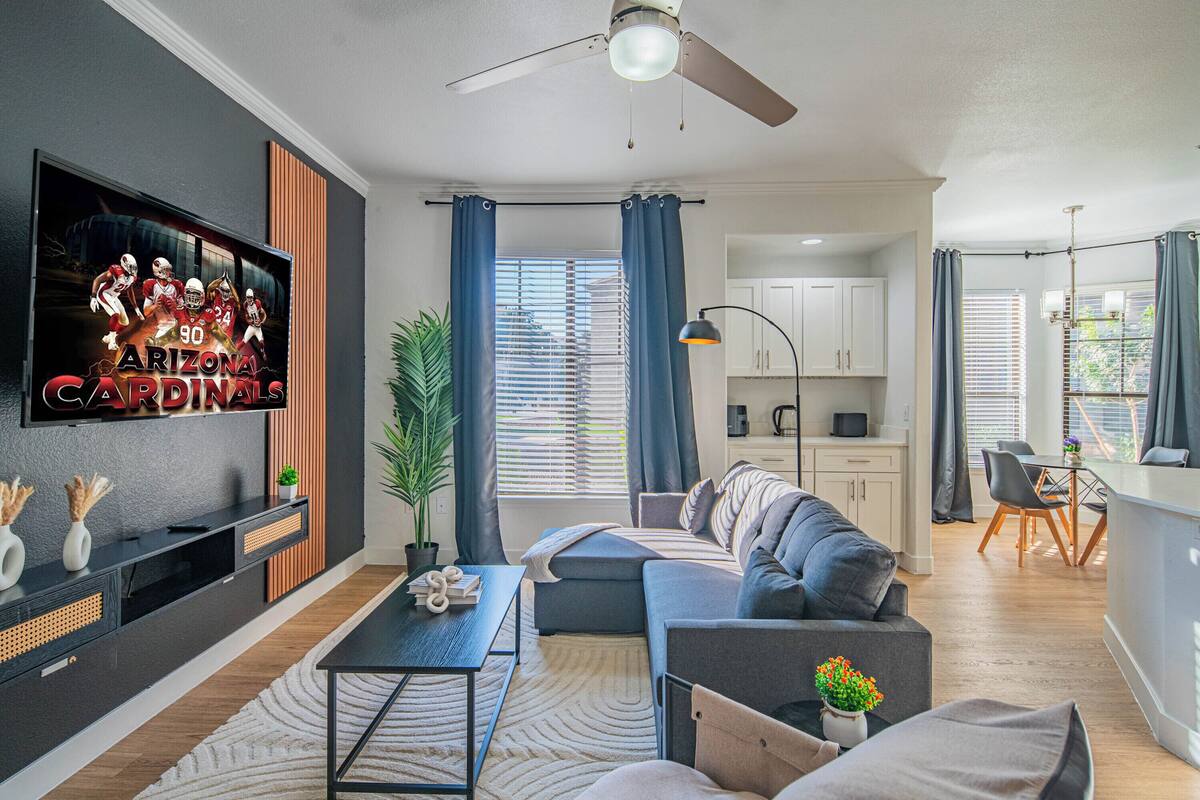 Een moderne woonkamer met een flatscreen televisie, een plafondventilator, een bank, een salontafel en een eethoek met een tafel en stoelen.