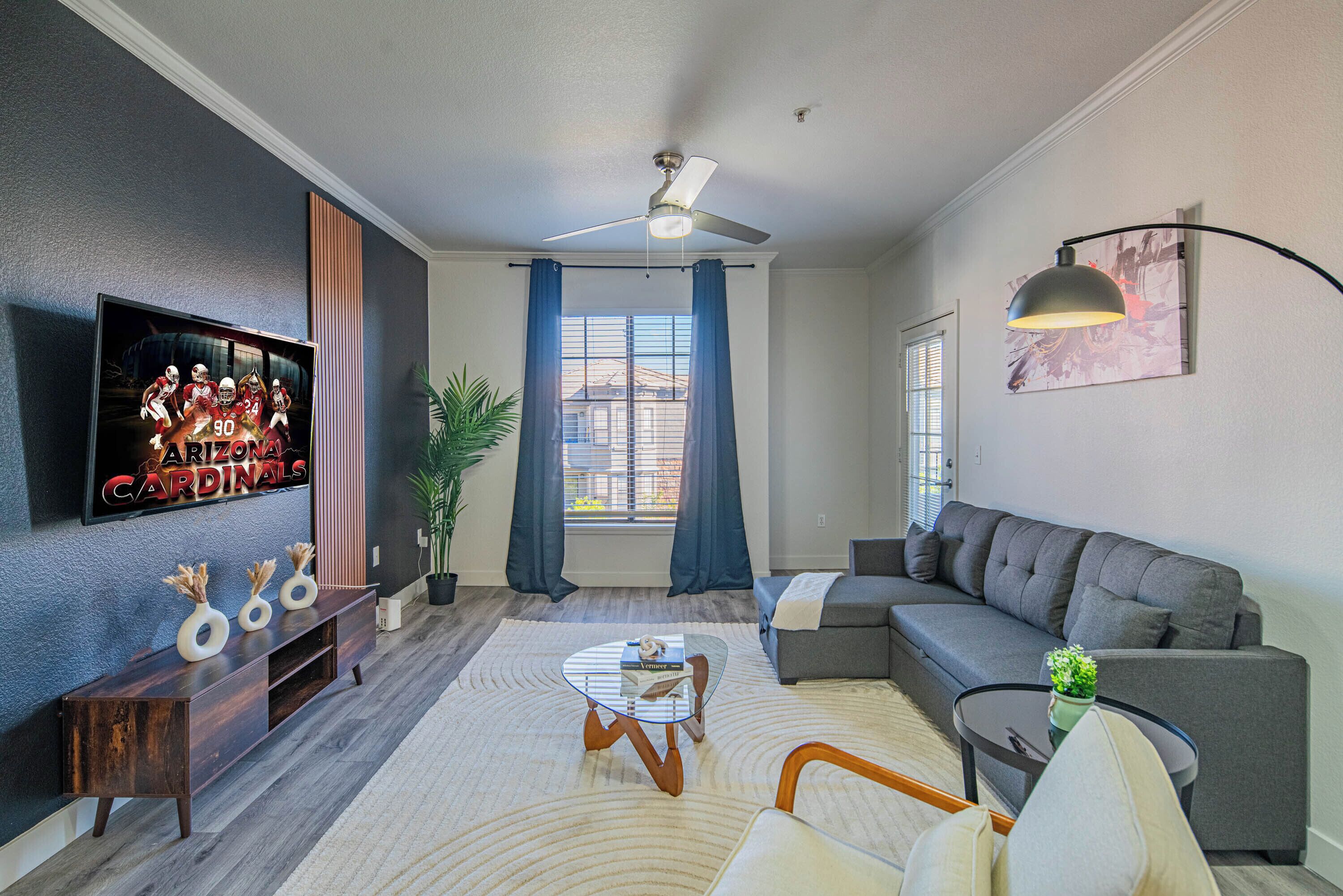 A modern living room with a flat-screen TV, a ceiling fan, a sofa, a coffee table, and a potted plant.