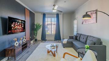 A modern living room with a flat-screen TV, a ceiling fan, a sofa, a coffee table, and a potted plant.
