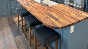Eine moderne Küche mit einer zentralen Kochinsel, dunkelblauen Schränken, Edelstahlgeräten und einer Holz Arbeitsplatte.