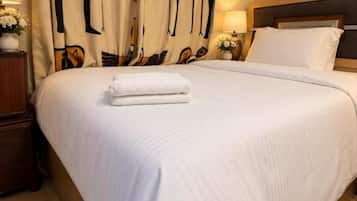 A neatly made bed with white linens, a pair of slippers on the floor, and a curtain with a bird pattern.