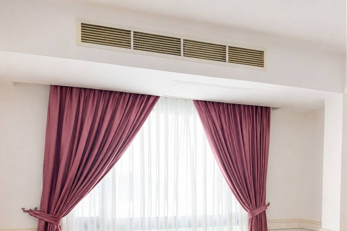 A hotel room with a bed, two pink armchairs, a small round table, and a large window with sheer curtains.