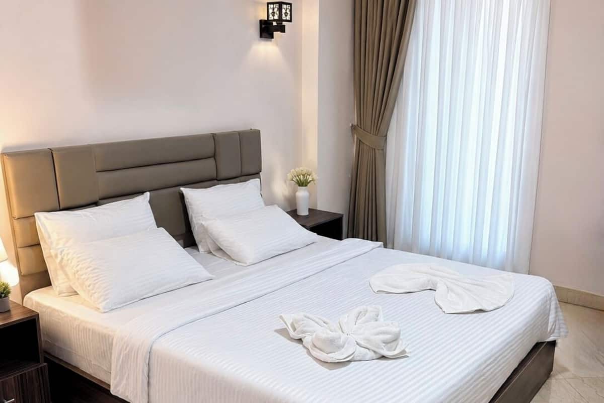 A hotel room with a large bed, a nightstand, a wall-mounted lamp, and a window with curtains.