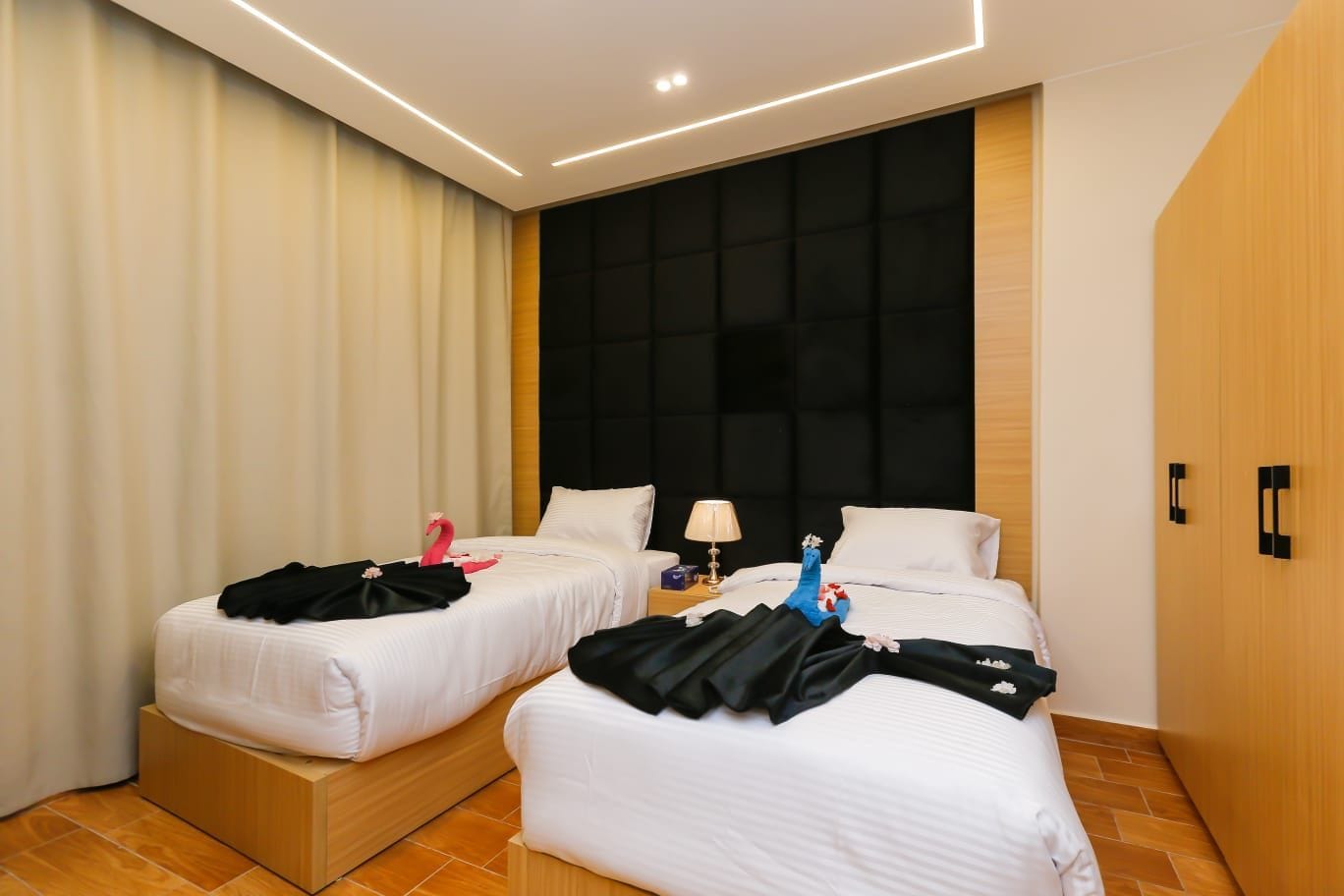 A hotel room with two beds, a nightstand with a lamp, and a large window with curtains.