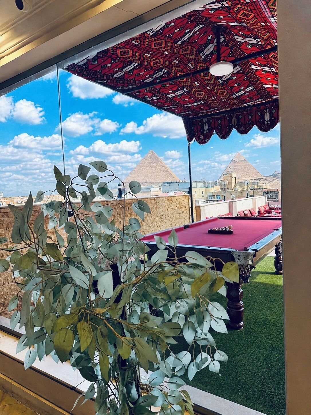 A pool table with a view of pyramids through a window.