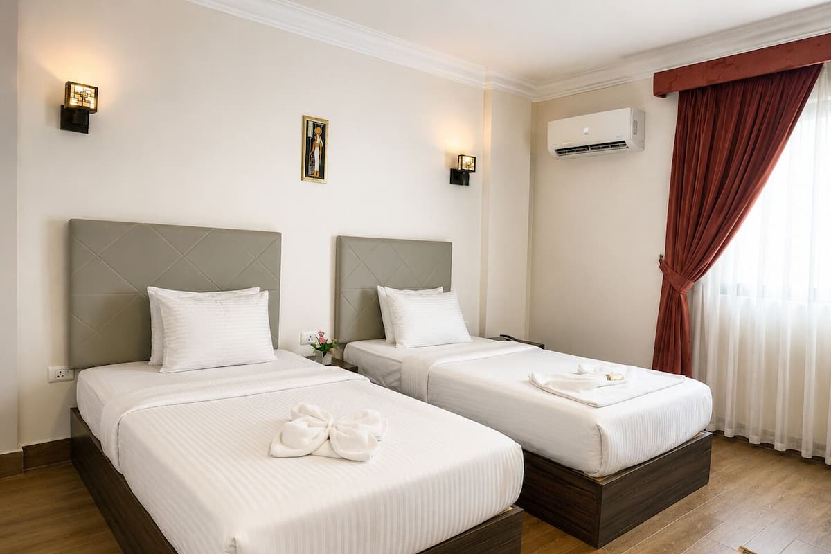 A hotel room with two beds, a wall-mounted air conditioner, and a window with curtains.