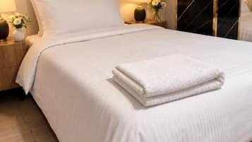 A neatly made bed with a folded white towel, two bedside lamps, and a pair of slippers on the floor.