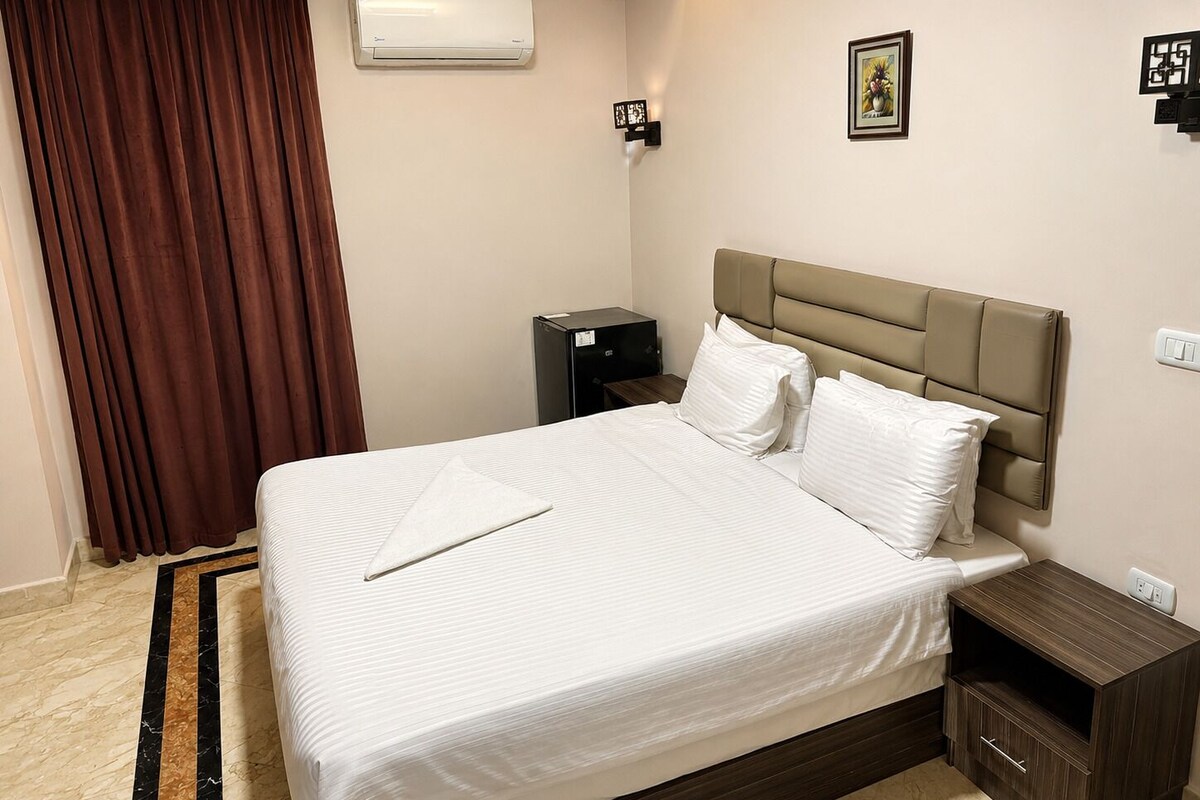 Habitación de hotel con cama, mesita de noche, cómoda, unidad de aire acondicionado, marco de foto y cortina.