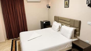 A hotel room with a bed, a nightstand, a dresser, an air conditioning unit, a picture frame, and a curtain.
