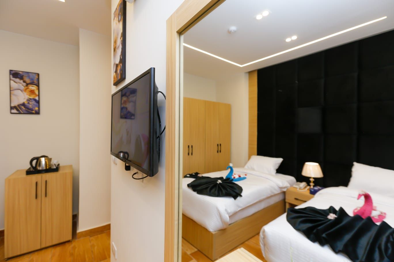 A hotel room with a bed, a TV mounted on the wall, a wardrobe, and a bedside table with a lamp.