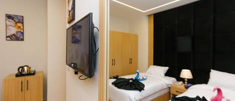 A hotel room with a bed, a TV mounted on the wall, a wardrobe, and a bedside table with a lamp.