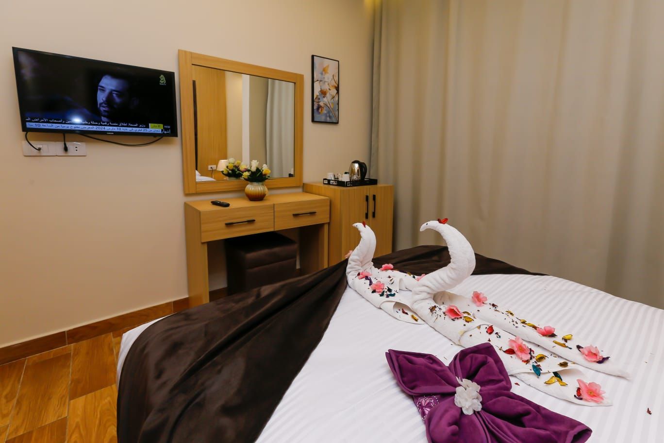 A hotel room with a bed, a TV, a desk, a mirror, and a window with curtains.
