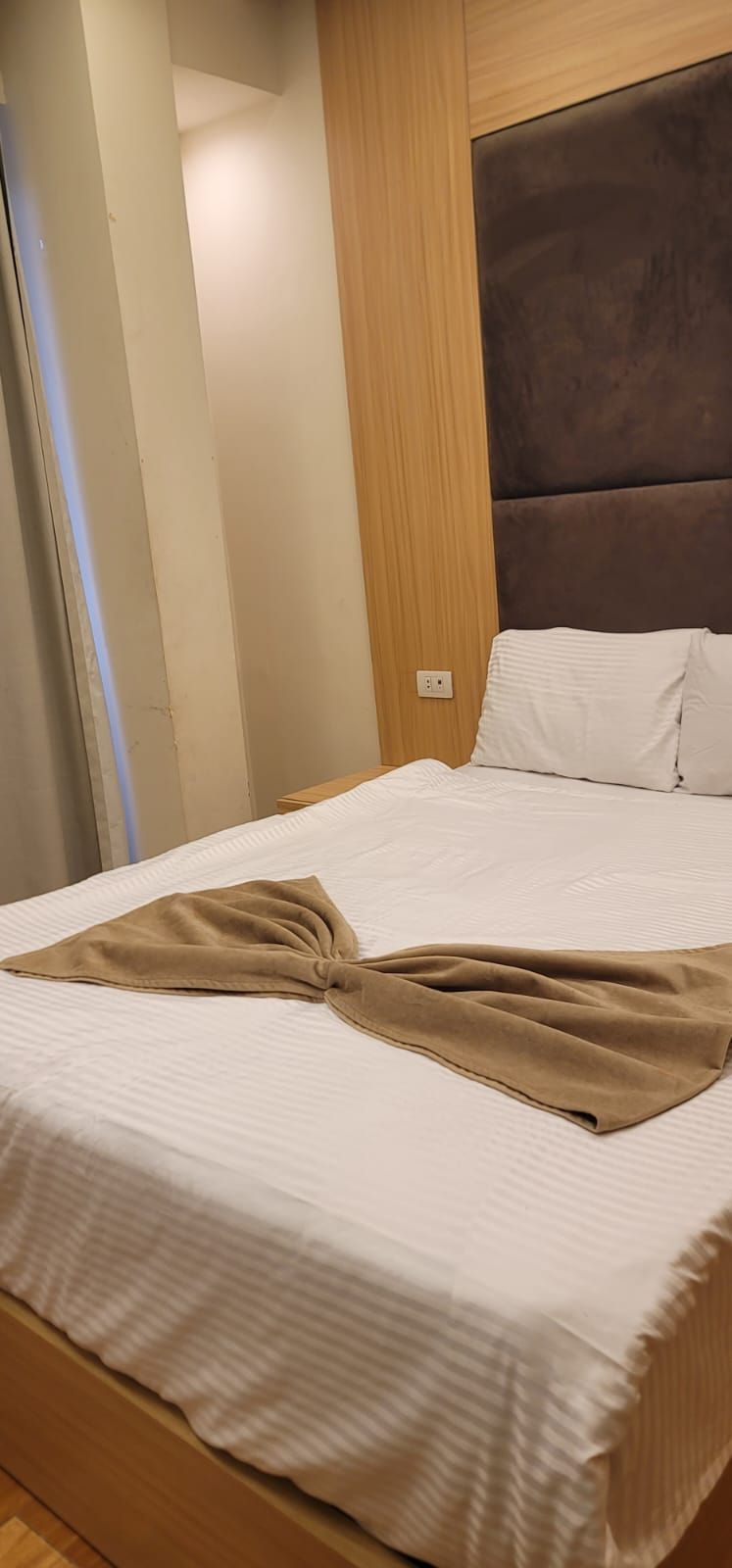 Uma cama com cobertor marrom, cabeceira de madeira e travesseiro branco.
