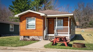 Une petite cabane en rondins avec un porche, une porte d’entrée et une boîte aux lettres.