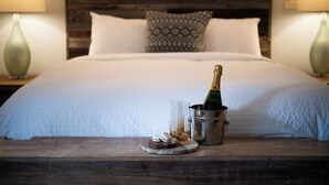 A neatly made bed with a wooden headboard, a bottle of champagne, and a glass on a wooden nightstand. - The Wakefield Grand (Wakefield)