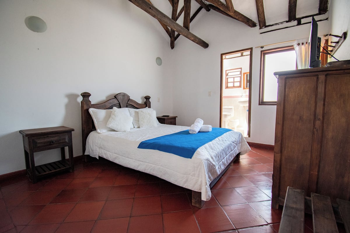 Ein Schlafzimmer mit einem hölzernen Bett, weißer Bettwäsche, einer blauen Decke und einem Nachttisch aus Holz.
