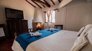 Ein Schlafzimmer mit einem großen Bett, einem Fernseher, einem Kamin und einem Fenster mit Vorhängen.