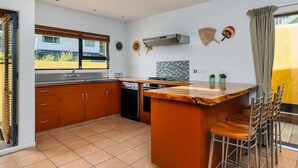 Une cuisine moderne dotée d’un îlot central, de meubles en bois, d’un four encastré et d’une fenêtre donnant sur un jardin.