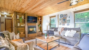 Una sala de estar acogedora con chimenea, paredes de madera y un ventanal con vistas al bosque.