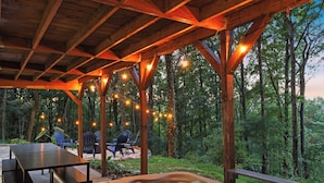 Un área de hidromasaje al aire libre con vigas de madera y luces colgantes, rodeada de árboles.