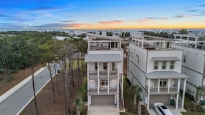 A multi-story residential building with a central entrance, balconies, and a view of the sea at sunset. - Rooftop Deck w/ Ocean View, Pool, Walk to Beach! Coastal Canopy by Avantstay (Panama City Beach)