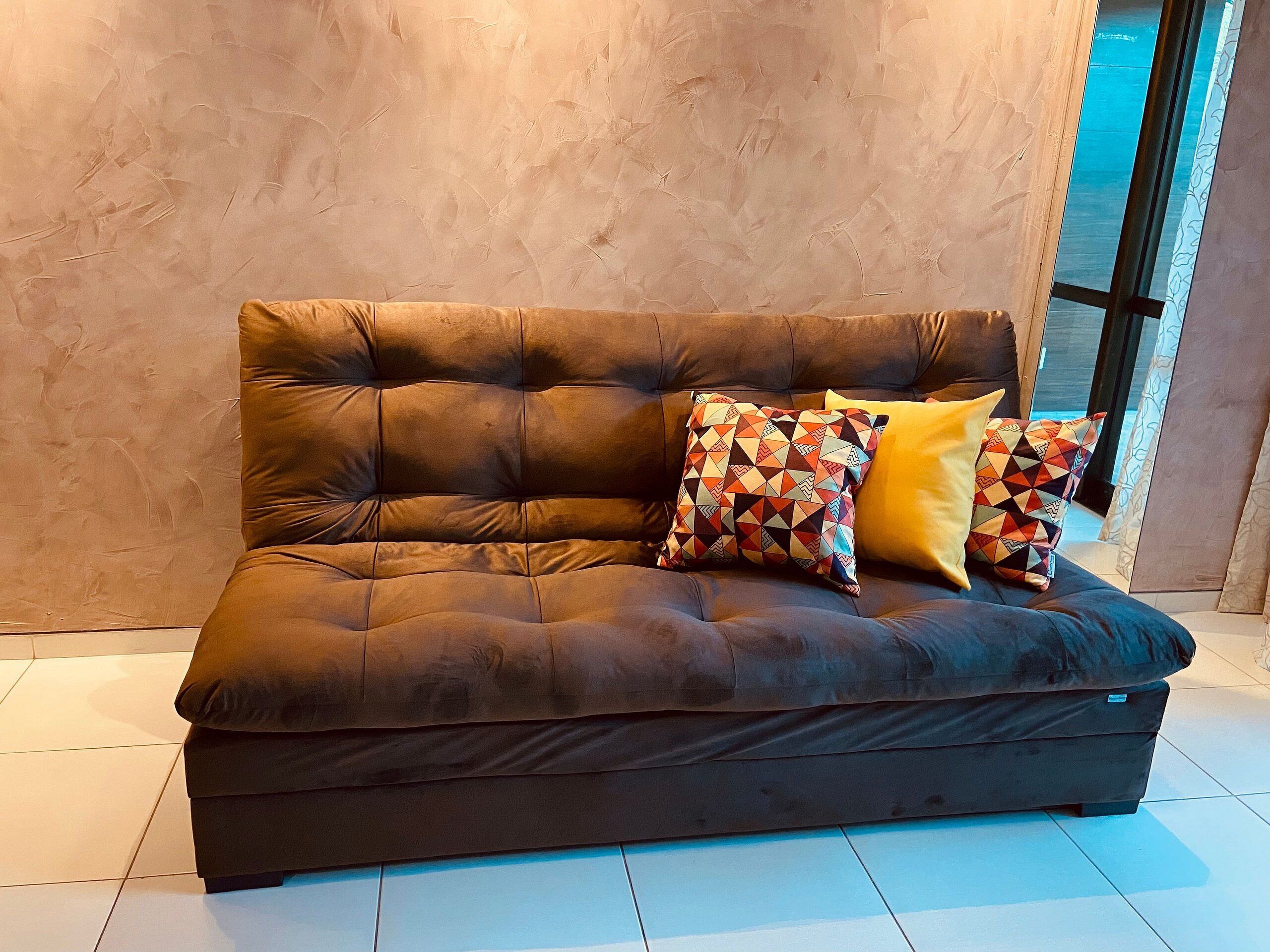Ein dunkelbraunes Sofa mit einer gepolsterten Struktur, zwei gemusterte Kissen und ein schlichtes gelbes Kissen.