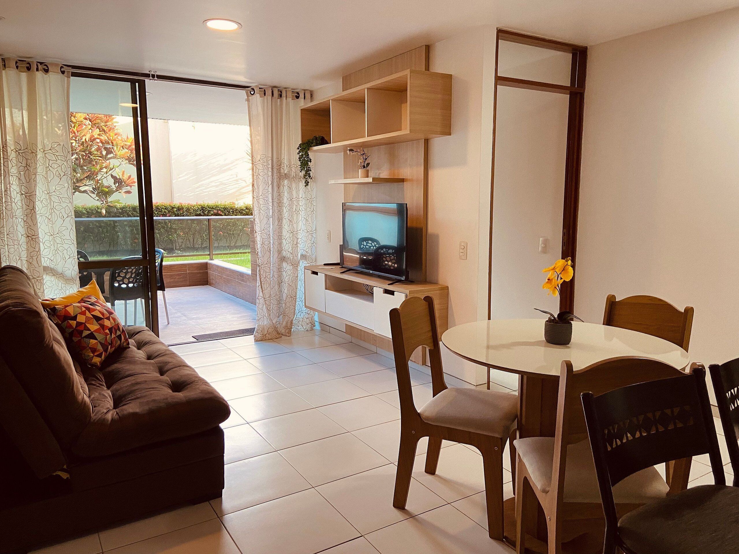 Een woonkamer met een bank, televisie en een eettafel met stoelen.