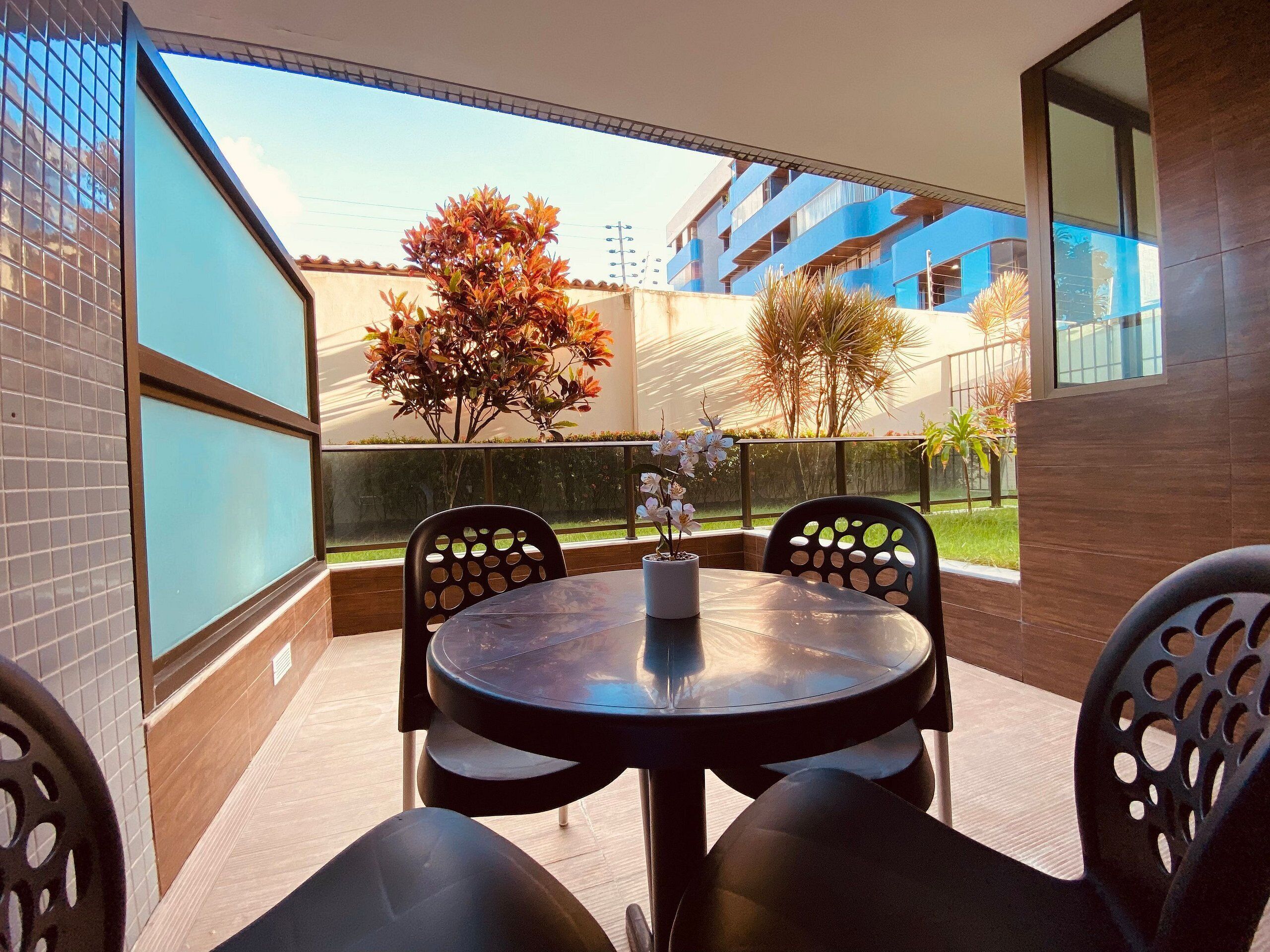 A balcony with a round table and chairs, a potted plant, and a view of a building with blue balconies.