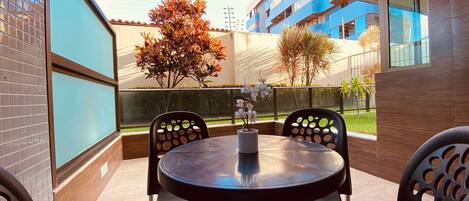 A balcony with a round table and chairs, a potted plant, and a view of a building with blue balconies.