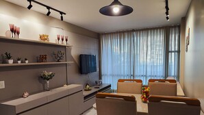 Una cocina moderna con comedor, que incluye un televisor de pantalla plana, una mesa de comedor con sillas y un ventanal con cortinas.