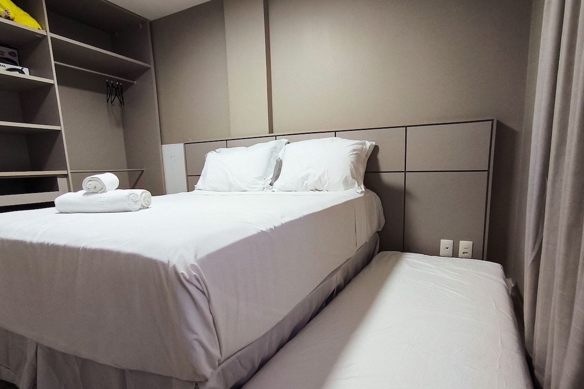 A hotel room with a large bed, a smaller bed, a wardrobe, and a shelf with towels.