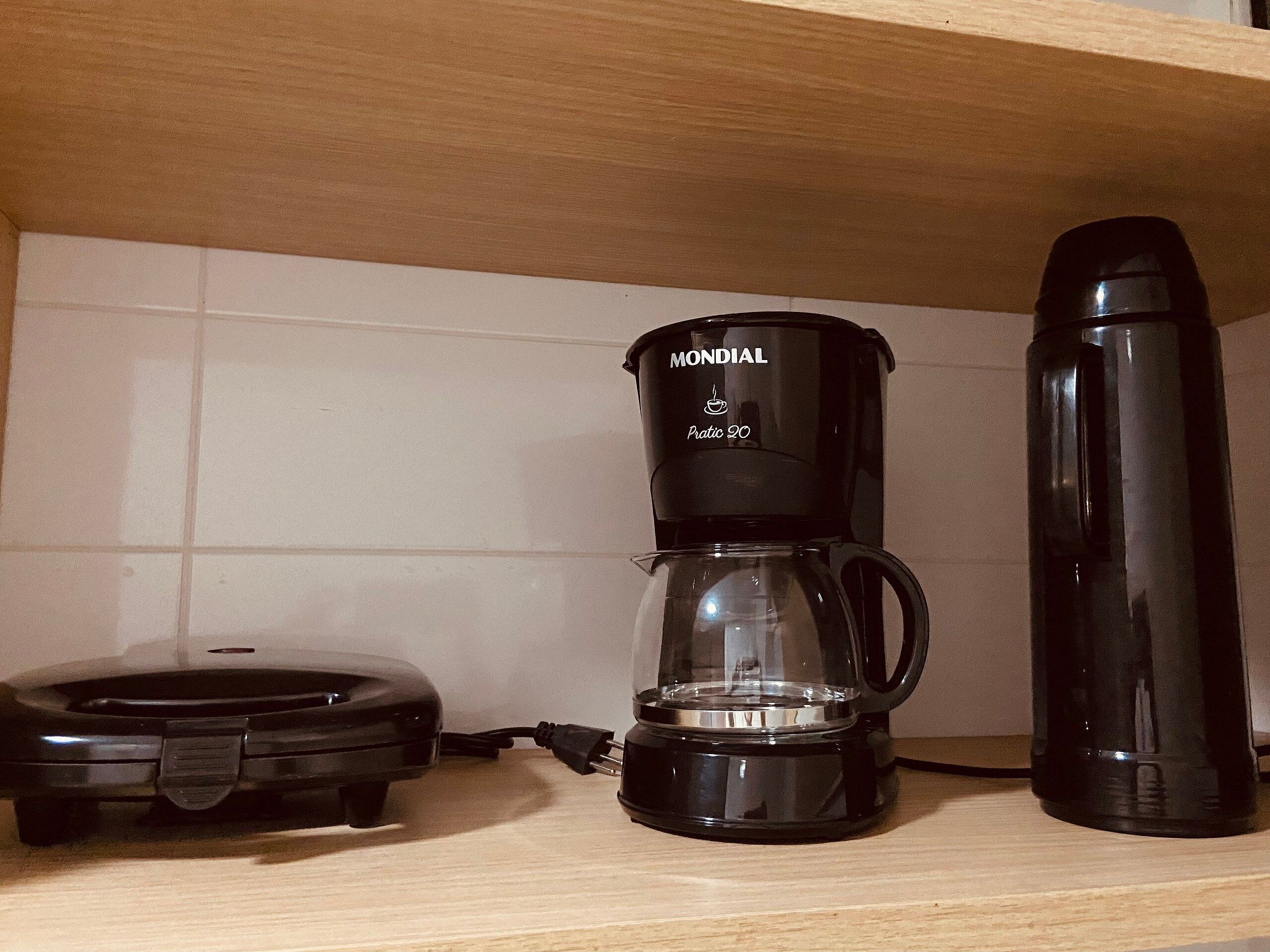 A kitchen with a coffee maker, a thermos, and a food warmer on the counter.