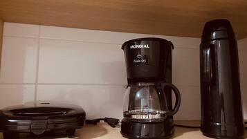 A kitchen with a coffee maker, a thermos, and a food warmer on the counter.
