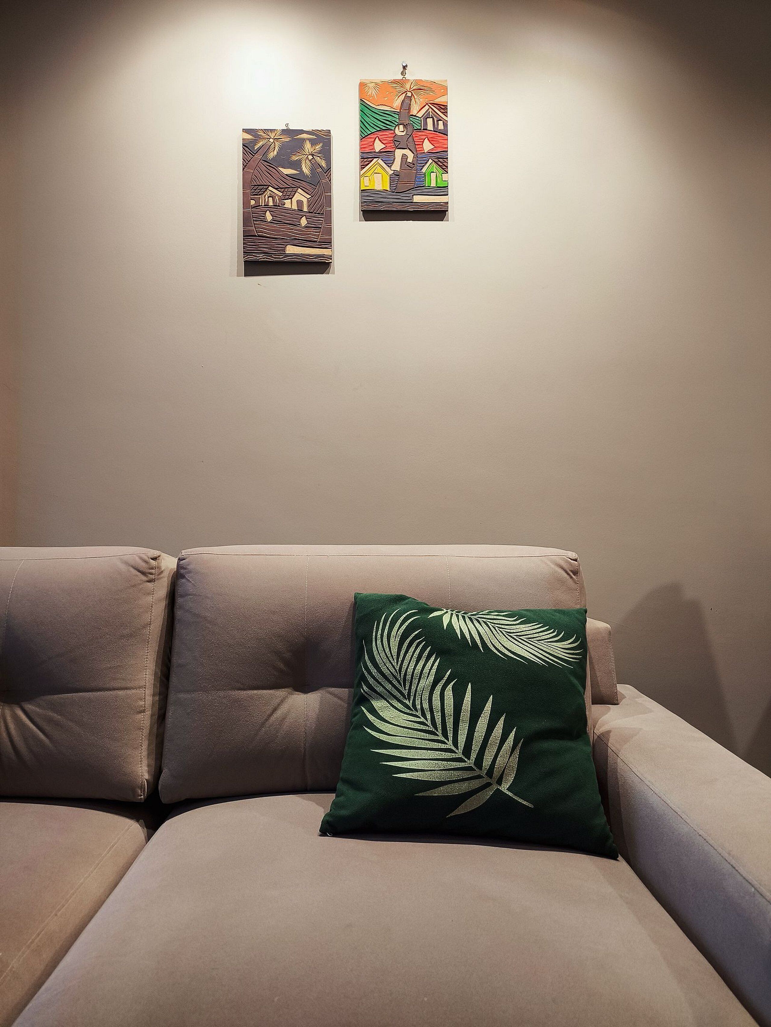 A living room with a beige sofa and a green pillow with a leaf pattern. There are two framed artworks on the wall.