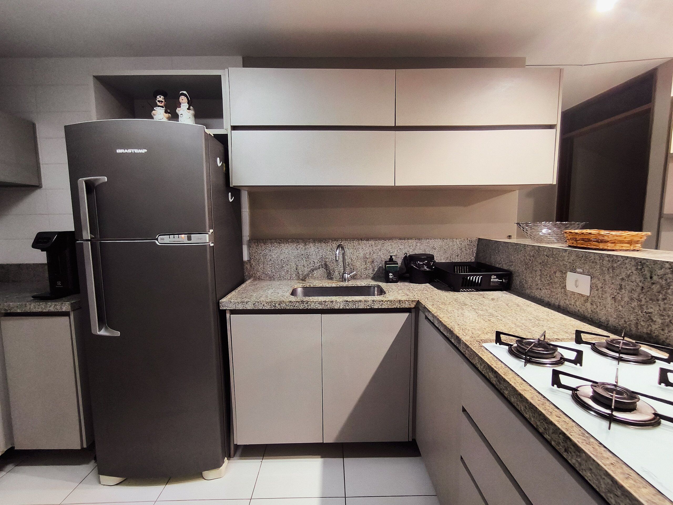 Una cocina moderna con un refrigerador de acero inoxidable, una encimera de granito, un lavamanos y una estufa a gas.
