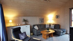 Un salon chaleureux avec un canapé, deux fauteuils, une table basse en bois et un petit coin cuisine doté d’un comptoir et de placards.